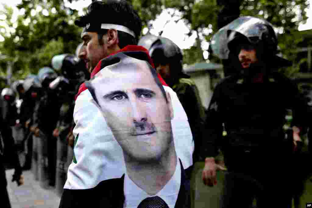 A Syrian man wrapped in a Syrian flag with a portrait of President Bashar Assad, walks past anti-riot police during an anti-Israeli demonstration in front of the U.N. office in Tehran, Iran. Iran condemns Israeli air strikes on Syria and urged countries in the region to stand against the attack.