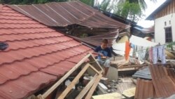 Seorang anak sedang makan diatas puing bangunan rumah yang roboh di desa Kayuangi, Kecamatan Malunda, Kabupaten Majene, Sulawesi Barat. Jumat (28/1/2021). (Foto: VOA/Yoanes Litha)