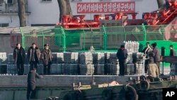 FILE - North Korean men unload goods off a boat on the river bank of the North Korean town of Sinuiju, opposite side of Chinese city of Dandong bordering with North Korea, Dec. 30, 2011.