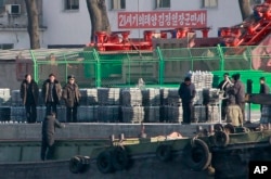 FILE - North Korean men unload goods off a boat on the river bank of the North Korean town of Sinuiju, opposite side of Chinese city of Dandong bordering with North Korea, Dec. 30, 2011.