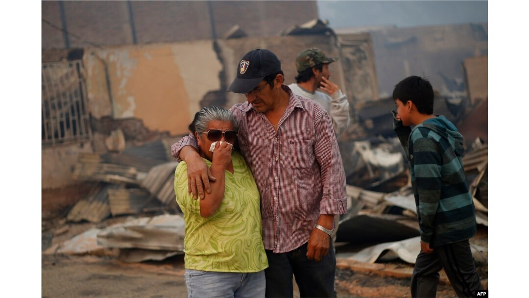 A crying woman is comforted amid the remains of a burnt-down house after a forest fire devastated Santa Olga, 240 kilometers south of Santiago, Chile, Jan. 26, 2017.