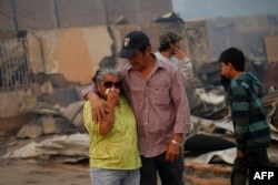 A crying woman is comforted amid the remains of a burnt-down house after a forest fire devastated Santa Olga, 240 kilometers south of Santiago, Chile, Jan. 26, 2017.
