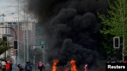 Los manifestantes se paran junto a una barricada en llamas cuando el aumento en el transporte público llevó al presidente Sebastián Piñera a declarar el estado de emergencia en Concepción, Chile, el 20 de octubre de 2019.