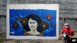 FILE - A motorcyclist rides past a mural of slain environmentalist and indigenous leader Berta Caceres in Tegucigalpa, Honduras.