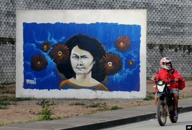 FILE - A motorcyclist rides past a mural of slain environmentalist and indigenous leader Berta Caceres in Tegucigalpa, Honduras.
