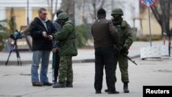 FILE - Armed men check journalists' documents around the regional parliament building in the Crimean city of Simferopol, March 1, 2014. 