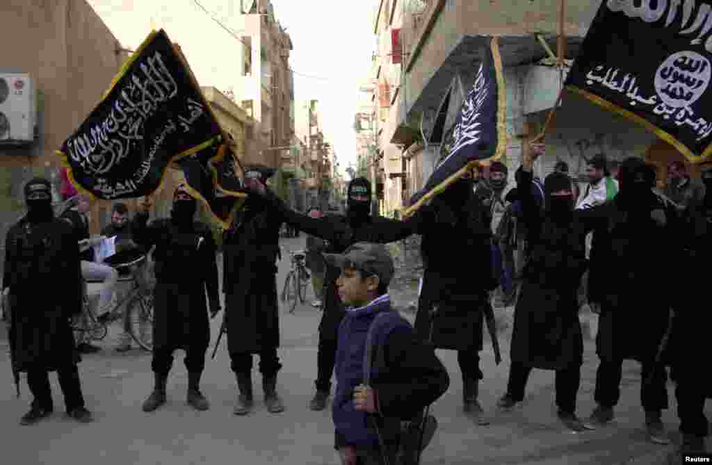 A boy walks past members of an Islamist group as they hold flags during a protest against Syrian President Bashar al-Assad&#39;s regime in Deir el-Zor, Syria, Feb. 25, 2013.