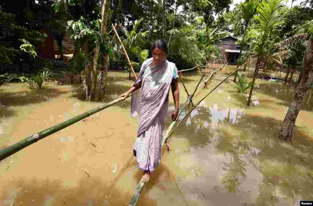 Seorang perempuan desa melewati &#39;jembatan bambu&#39; untuk menyeberangi jalanan yang tergenang banjir di distrik Nagaon, negara bagian Assam, India.
