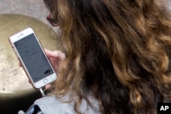 FILE - A woman uses a ride-hailing app while waiting for a ride outside Grand Central Terminal in New York, Aug. 1, 2018.