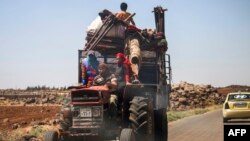 A Syrian family rides with belongings on a tractor-drawn trailer as they flee from fighting in the southern Syrian province of Daraa, June 21, 2018.