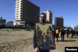 FILE - A man holds an icon against the backdrop of crumbling buildings destroyed in Cyprus's 1974 war during a celebration for Orthodox Epiphany for the first time in decades at Famagusta, Cyprus, Jan. 6, 2016.