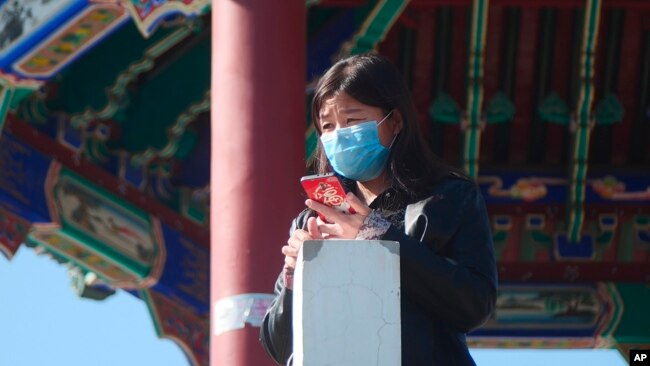 A woman wearing a face mask stands at a pagoda in Ritan Park in Beijing, Tuesday, Feb. 18, 2020. (AP Photo/Sam McNeil)