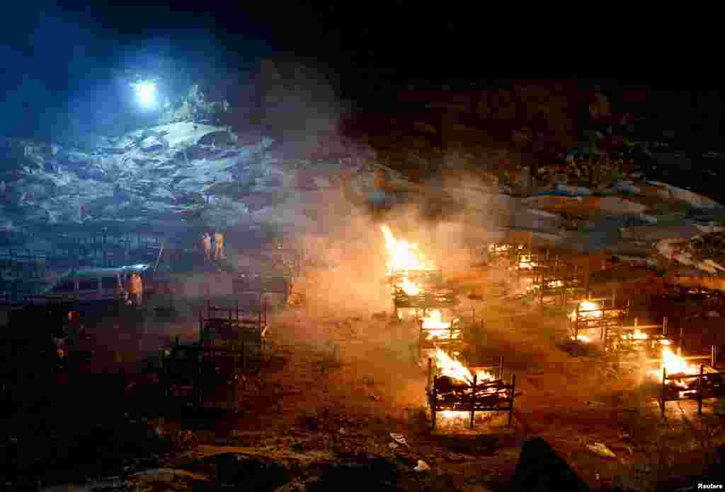 Volunteers stand next to burning pyres of people who died due to the COVID-19, at a crematorium ground in Giddenahalli village on the outskirts of Bengaluru, India, May 2, 2021.