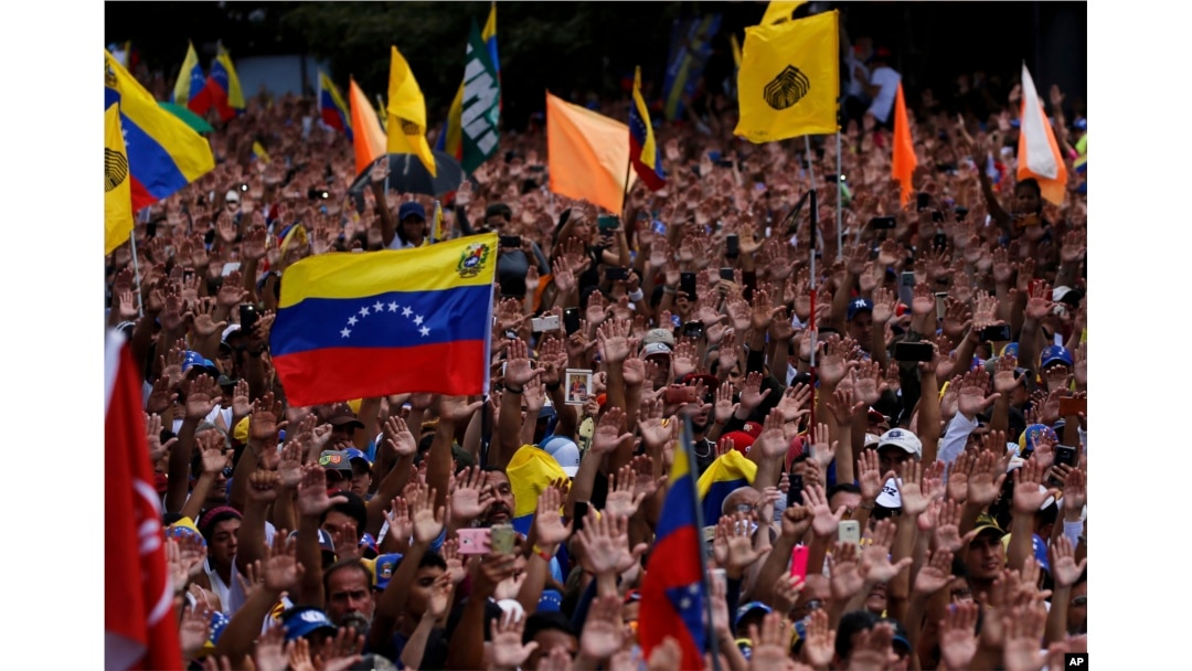 Anti-government protesters hold their hands up during the symbolic swearing-in of Juan Guaido, head of the opposition-run congress who declared himself interim president of Venezuela.