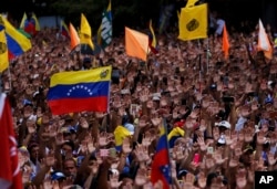 Anti-government protesters hold up their hands up during the symbolic swearing-in of Juan Guaido, head of the opposition-run National Assembly, who declared himself interim president of Venezuela, during a rally demanding President Nicolas Maduro's resignation, in Caracas, Venezuela, Jan. 23, 2019.