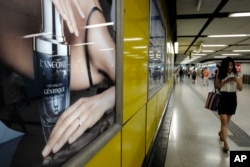 FILE - A woman walks past a Lacome advertisement at a subway station in Hong Kong, June 7, 2016.