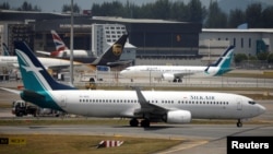 A SilkAir Boeing 737 Max 8 plane (behind) sits on the tarmac near a hangar after suspended operations for all Boeing 737 Max 8 planes, at Changi Airport in Singapore, March 12, 2018.