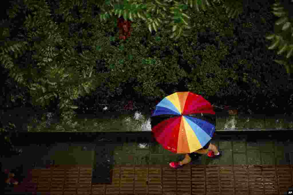 A woman carries a rainbow-colored umbrella as she walks during a rain shower in Beijing, China.