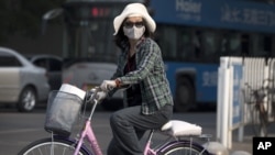 A Chinese woman wearing a face mask on a bicycle waits to cross a street in Beijing, May 31, 2013. 