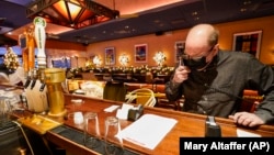 Steve Olsen, the owner of the West Bank Café, reads the specials over the phone to a customer in the empty restaurant. Photo taken on Saturday, Jan. 9, 2021. (AP Photo/Mary Altaffer)