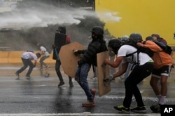 Anti-government protesters take cover from a water canon fired by security forces blocking a student march from reaching the Education Ministry in Caracas, Venezuela, May 8, 2017.