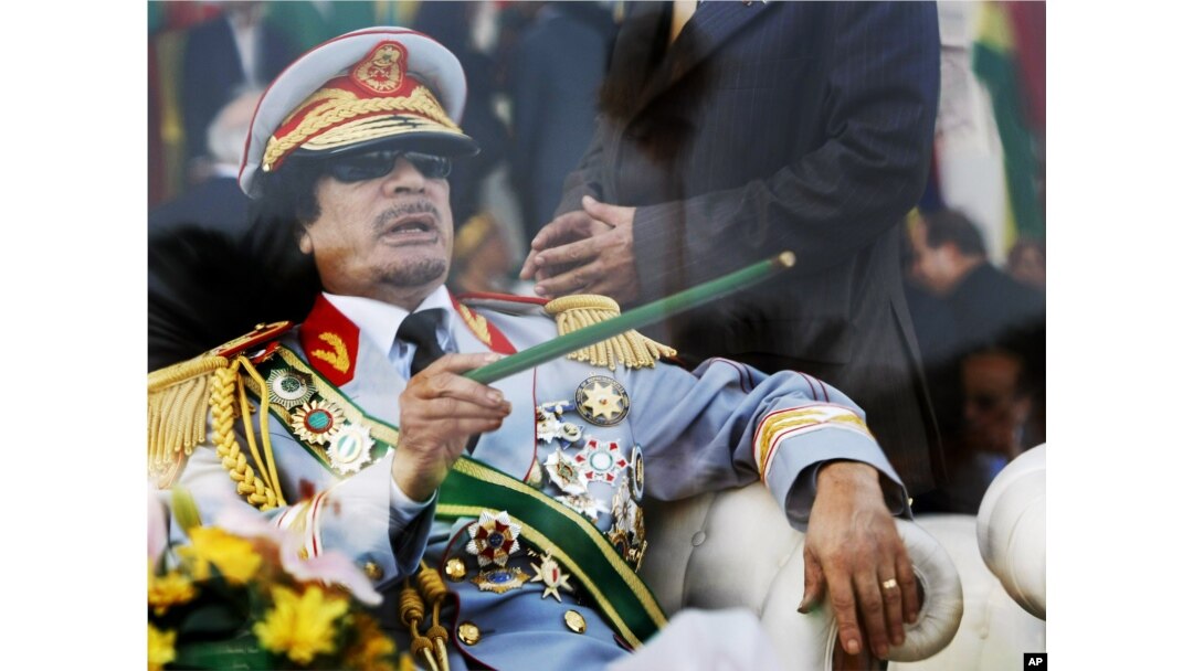 FILE - In this Tuesday, Sept. 1, 2009 file photo, Libyan leader Moammar Gadhafi gestures with a green cane as he takes his seat behind bulletproof glass for a military parade in Green Square, Tripoli, Libya.