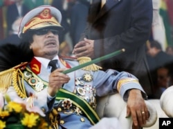 FILE - In this Tuesday, Sept. 1, 2009 file photo, Libyan leader Moammar Gadhafi gestures with a green cane as he takes his seat behind bulletproof glass for a military parade in Green Square, Tripoli, Libya.