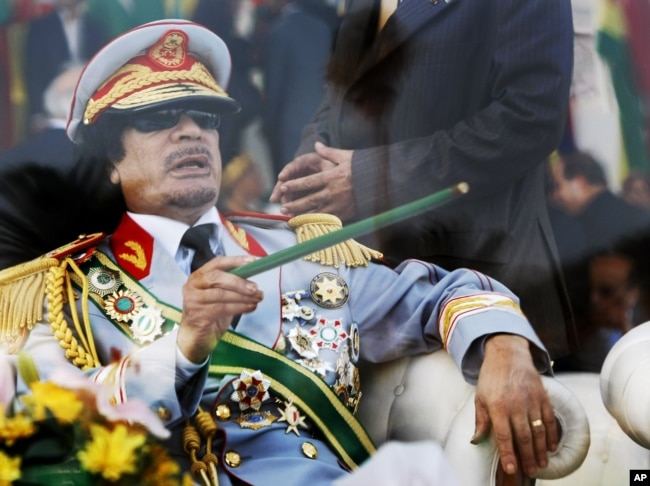 FILE - In this Tuesday, Sept. 1, 2009 file photo, Libyan leader Moammar Gadhafi gestures with a green cane as he takes his seat behind bulletproof glass for a military parade in Green Square, Tripoli, Libya.