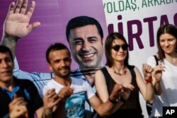 FILE - People dance in front of an election campaign poster of Selahattin Demirtas, a jailed pro-Kurdish politician and presidential candidate in Turkey's snap presidential poll, in Istanbul, June 5, 2018.