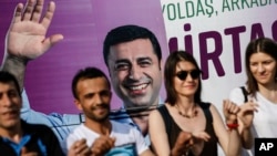 FILE - People dance in front of an election campaign poster of Selahattin Demirtas, a jailed pro-Kurdish politician and presidential candidate in Turkey's snap presidental poll, in Istanbul, June 5, 2018.