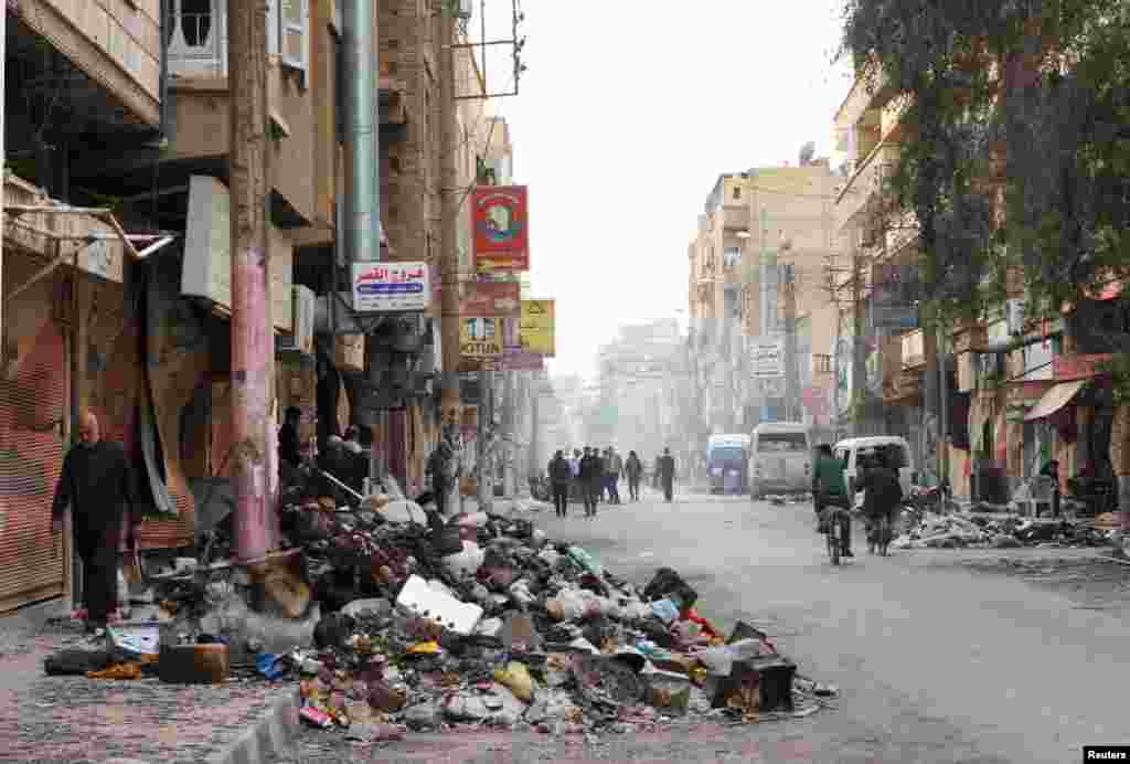 Residents walk past rubbish piled up along a street in Deir al-Zor, Syria, March 13, 2013.