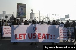 People hold a banner reading 'Let us eat' before marching down the street during a protest in Kabul, Afghanistan, Dec. 21, 2021, as the country struggles with a deep economic crisis.