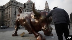 FILE - Man touches statue of a charging bull similar to New York's Wall Street Bull, in Shanghai, China, Feb. 7, 2012.