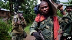 FILE - Congolese government army soldiers carry weapons and mortar equipment on the road to the border town of Bunagana, after their unit returned from the frontline of fighting against rebel forces, in Kinyamahura, Congo.