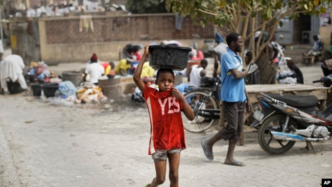 A young boy uses his shirt to dry the water dripping from the bucket onto his face, in Kano, northern Nigeria, Feb. 19, 2019.