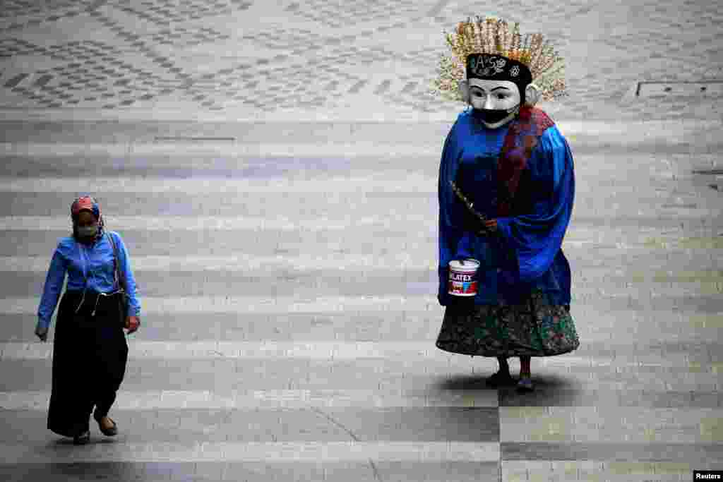 A traditional large puppet figure known as &quot;Ondel-ondel&quot;, wearing a face mask, performs on a sidewalk in Jakarta, Indonesia.