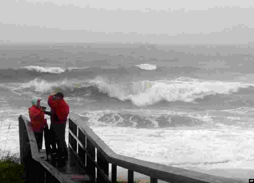 People watch the waves from the Atlantic Ocean in a rainstorm at Carolina Beach, North Carolina. Millions along the East Coast breathed a little easier Friday after forecasters said Hurricane Joaquin would probably veer out to sea instead of joining up with a drenching rainstorm that is bringing severe flooding.
