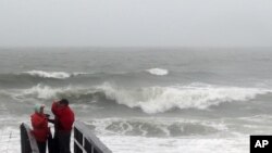 People watch the waves in a rainstorm at the Atlantic Ocean at Carolina Beach, North Carolina, Oct. 2, 2015.