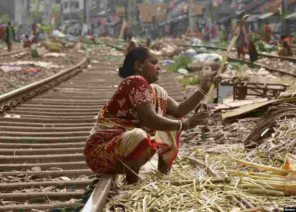 Seorang perempuan mengupas tebu di jalur kereta api untuk dijual pada pedagang air tebu di daerah kumuh di Kalkuta, India.