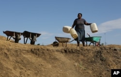 A woman arrives to collect stagnant rain water from an unfinished sewerage treatment tank, now used as a well, to do her laundry in Senekal, South Africa where taps and water sources have run dry, Jan. 7, 2016.