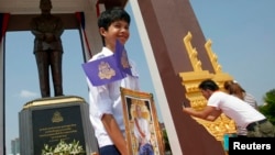 A student holds a portrait of Cambodia's King Norodom Sihamoni (C), after the unveiling ceremony of a statue (back) of the late King Norodom Sihanouk in central Phnom Penh, Oct. 11, 2013. 