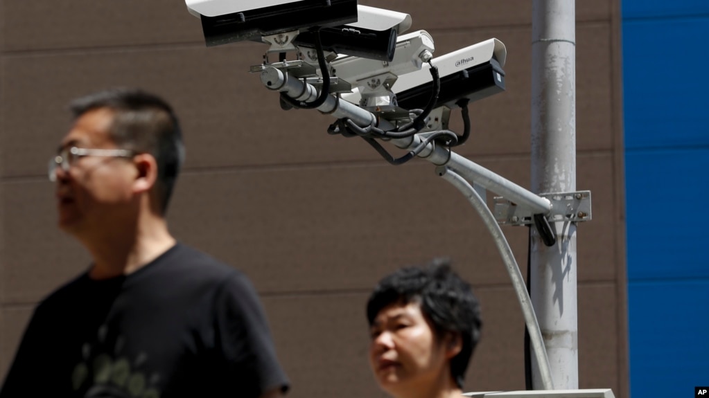 People walk by Chinese-made surveillance cameras installed along a street in Beijing, Thursday, May 23, 2019. The Chinese video surveillance company Hikvision says it is taking concern about the use of its technology.
