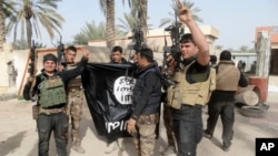 FILE - Iraqi security forces celebrate as they hold a flag of the Islamic State group they captured in Ramadi, Iraq. 