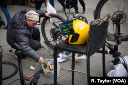 Zheng, a Chinese delivery worker, repairs his bike on a New York sidewalk.