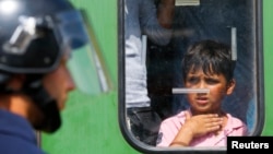 A migrant boy looks at a Hungarian policeman at the railway station in the town of Bicske, Hungary, Sept. 3, 2015. 