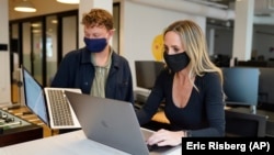 Kelly Soderlund, right, works with another employee at the TripActions office in San Francisco, Friday, Aug. 27, 2021. (AP Photo/Eric Risberg)