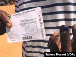 A voter shows her voter card and her finger marked with indelible ink after voting at the school Gobongo the 4th arrondissement, Bangui, Dec. 30, 2015.