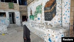FILE - A Palestinian woman walks outside her home, next to a house purchased by Jewish settlers, in the mostly Arab neighborhood of Silwan in east Jerusalem, October 2014.