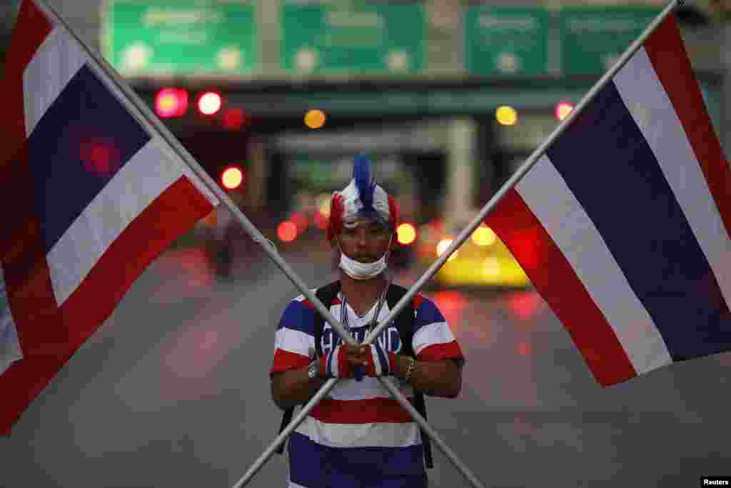 An anti-government protester holds two Thai flags as his group arrives to block one the of the major intersections of the city, Bangkok, Thailand, Jan. 12, 2014.