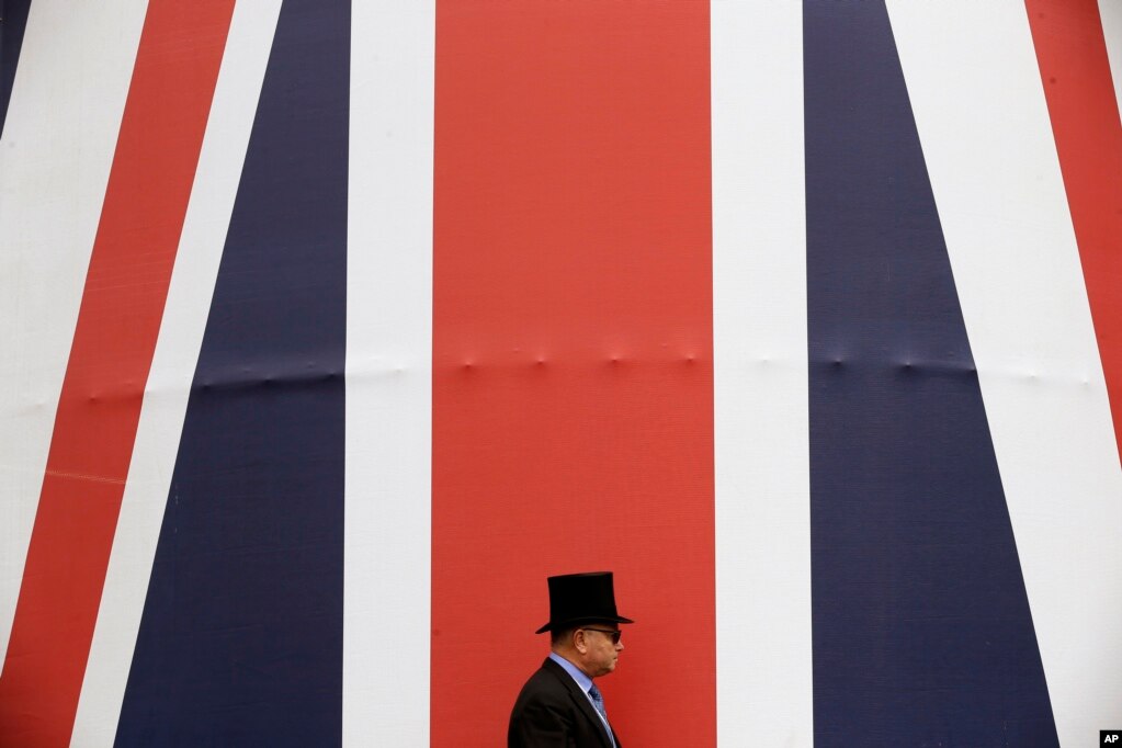 영국 전통의 경마 레이스인 '로얄 애스콧'에서 중년의 남성이 거대한 영국 국기 앞을 지나가고 있다.